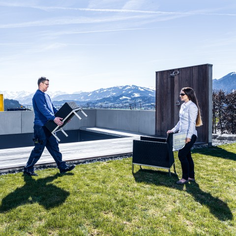 Livreur DACHSER portant un meuble de jardin sur une terrasse, accueilli par une cliente
