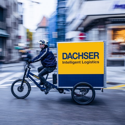 Coursier à vélo cargo DACHSER en livraison dans une rue de ville