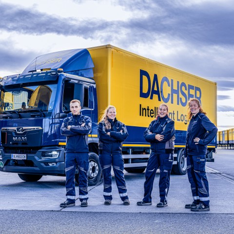 Quatre collaborateurs DACHSER en tenue de travail devant des camions DACHSER